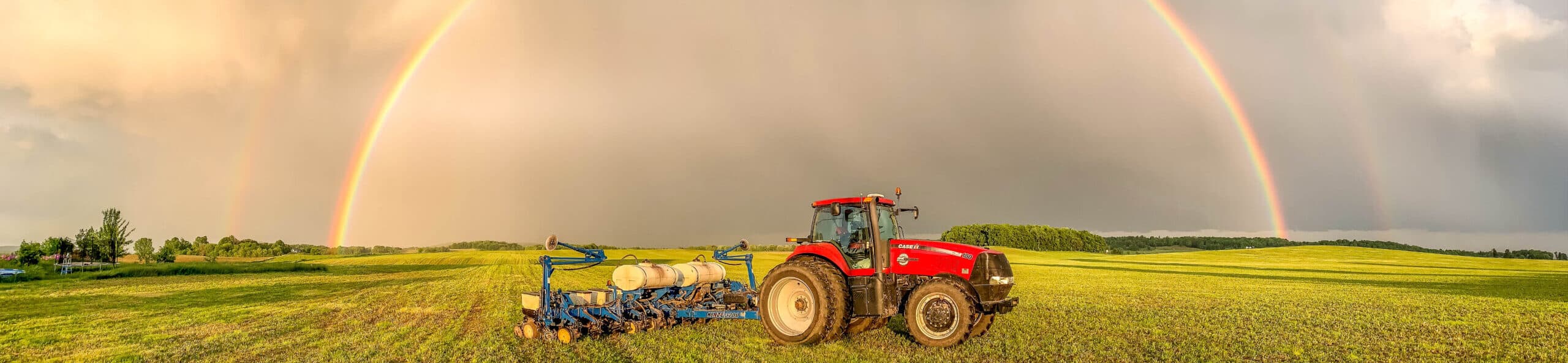 A tractor on a green field underneath a rainbow for Service Motors